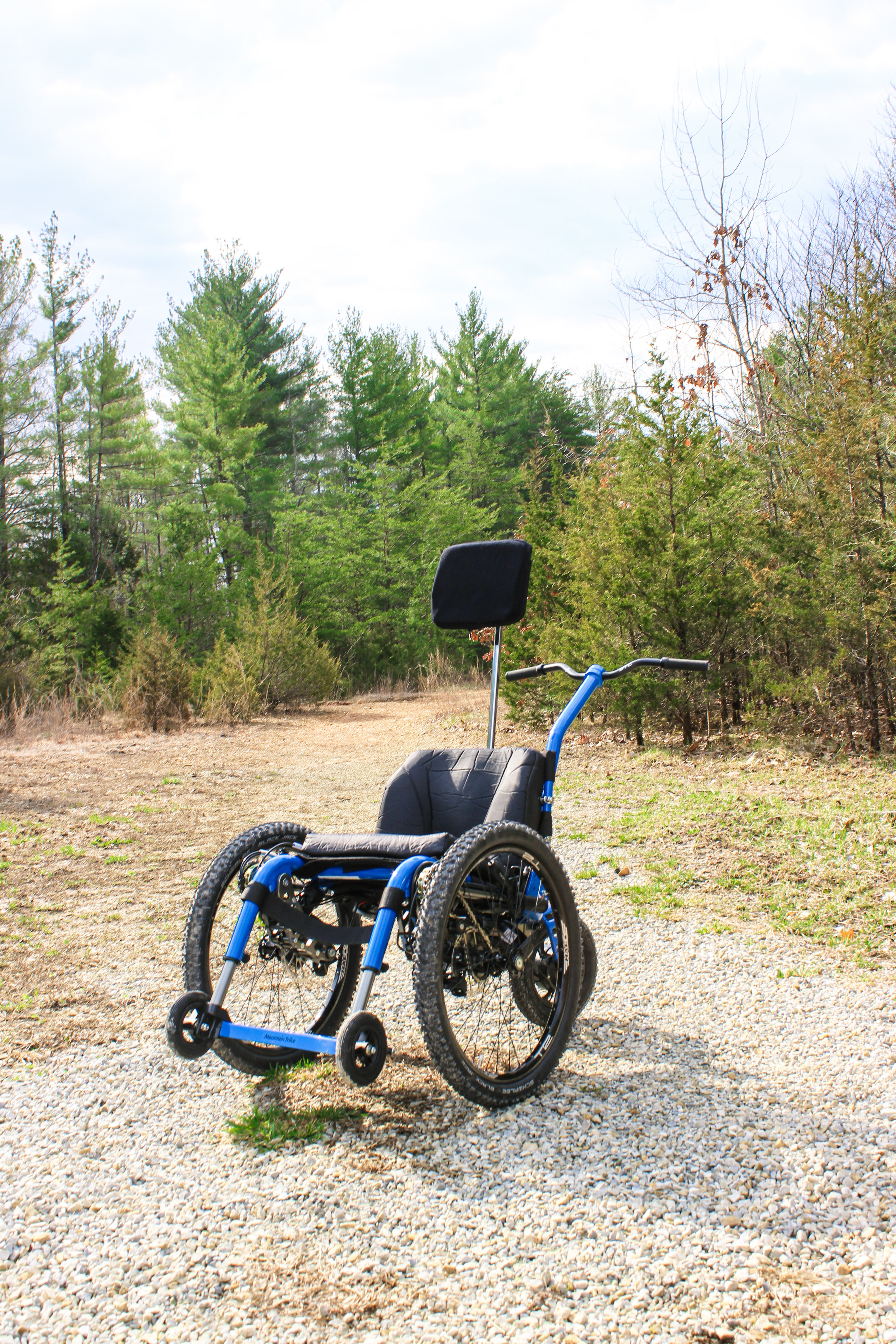 All-terrain wheelchair with high profile knobby tires sitting in an open space with pine trees in the background