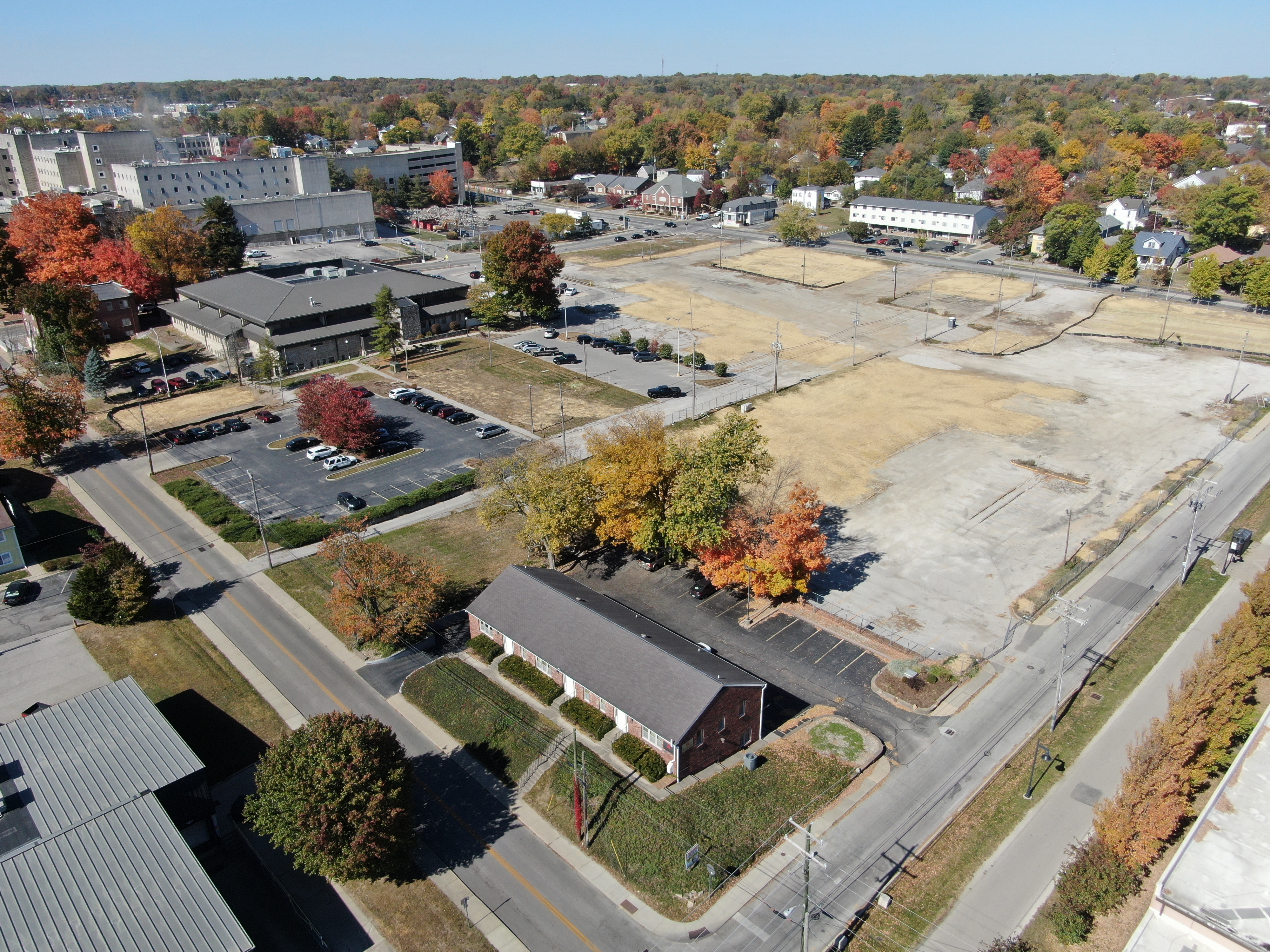 Aerial drone photo showing the completed demolition work.  The left photo is looking northwest from the intersection of 1st and Morton Street, showing a red brick office building with the site covered in straw in the background. 