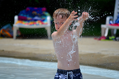 Young boy with upraised hands in pool fountain