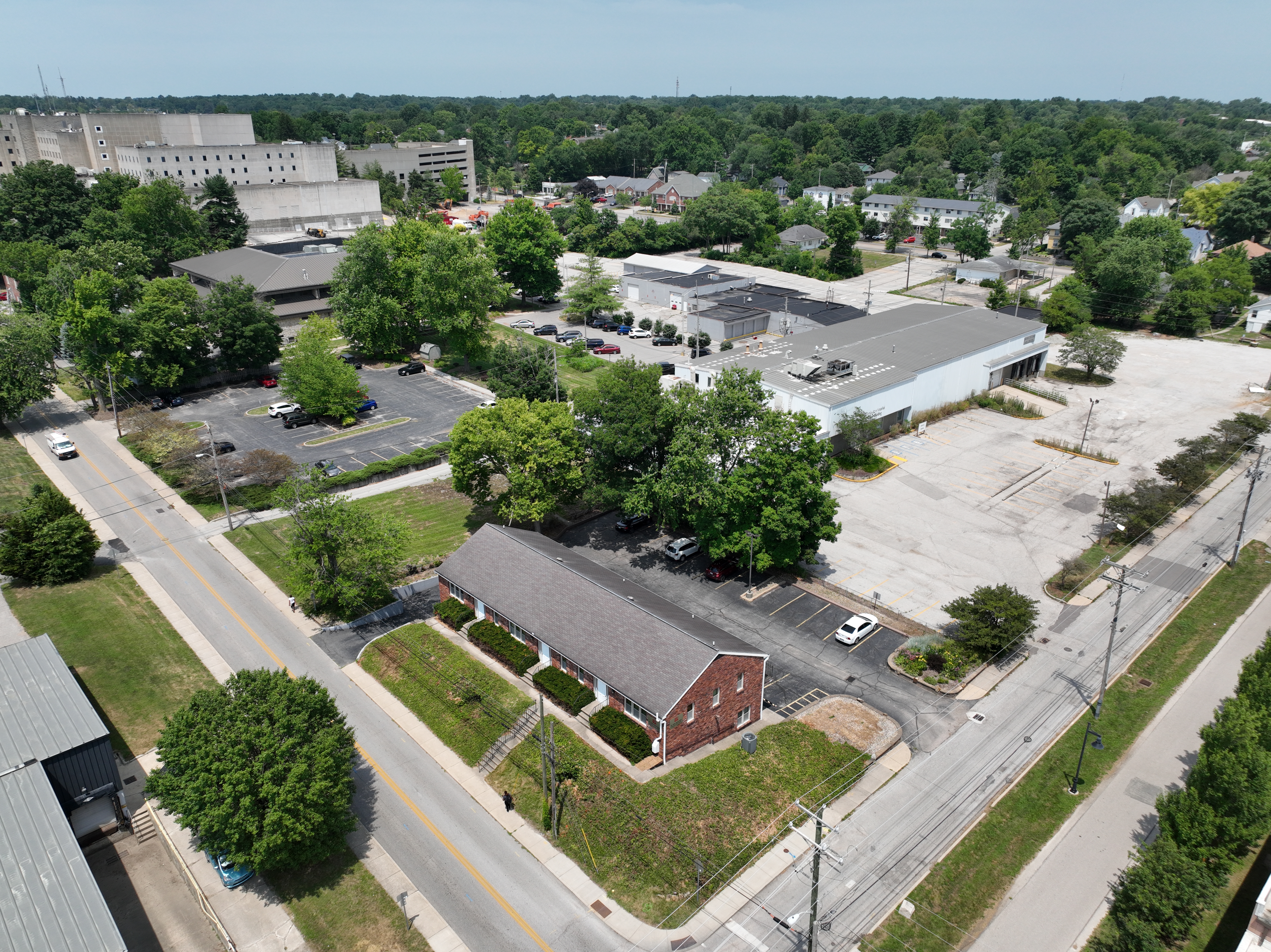 Aerial drone photo showing the development site prior to demolition. The left photo looks southwest from the intersection of 2nd and Morton Street, showing residential houses in the foreground with warehouses behind and the legacy hospital in the background. 