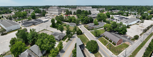 Aerial drone photo showing the development site prior to demolition. The left photo looks southwest from the intersection of 2nd and Morton Street, showing residential houses in the foreground with warehouses behind and the legacy hospital in the background. The right photo looks northwest from the intersection of 1st and Morton Street, showing a brick office building with warehouses and the legacy hospital in the background.