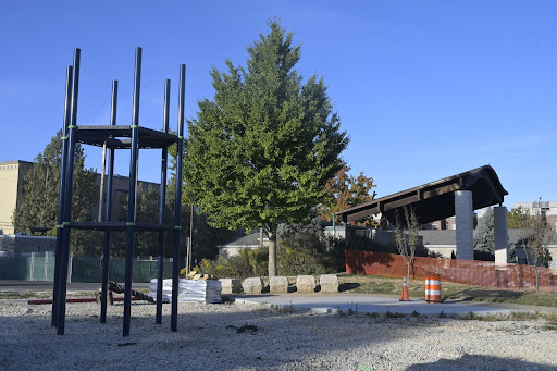 In the foreground is a newly installed two-tier six-sided climber.  In the background are a tree and the outdoor park scene, protected by a construction mesh fence. 