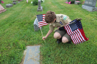 Scout placing American flag on grave of veteran