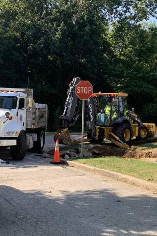 City dump truck and back hoe excavating ground for new ADA curb ramp.