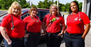 A photo showing four uniformed community care coordinators standing in front of a EMT vehicle