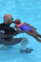 A man kneels in shallow water in a swimming pool to support a child who is learning to float