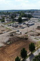 The right photo is looking southwest from the intersection of 2nd and Morton Street, there is a cleared site with exposed earth and the same equipment as the left photo working in the middle ground, the legacy hospital is shown in the background.