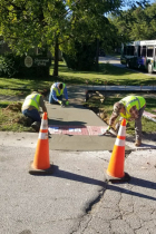 Three City workers in reflective safety vests install an ADA-compliant curb ramp on S Walnut Street Pike. 